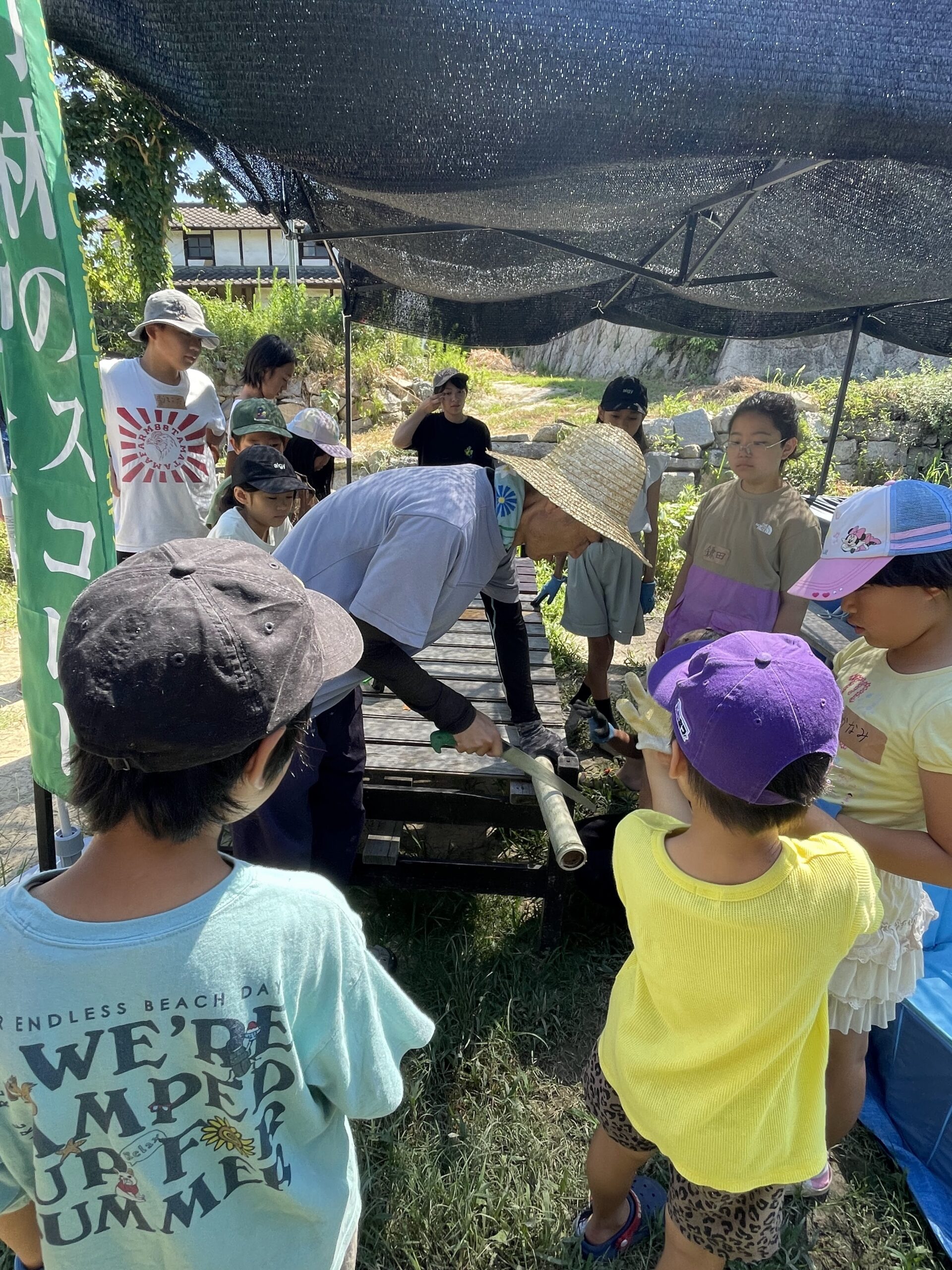 竹林のスコレーの旗の下、屋外で集まって話を聞く子どもたちの様子