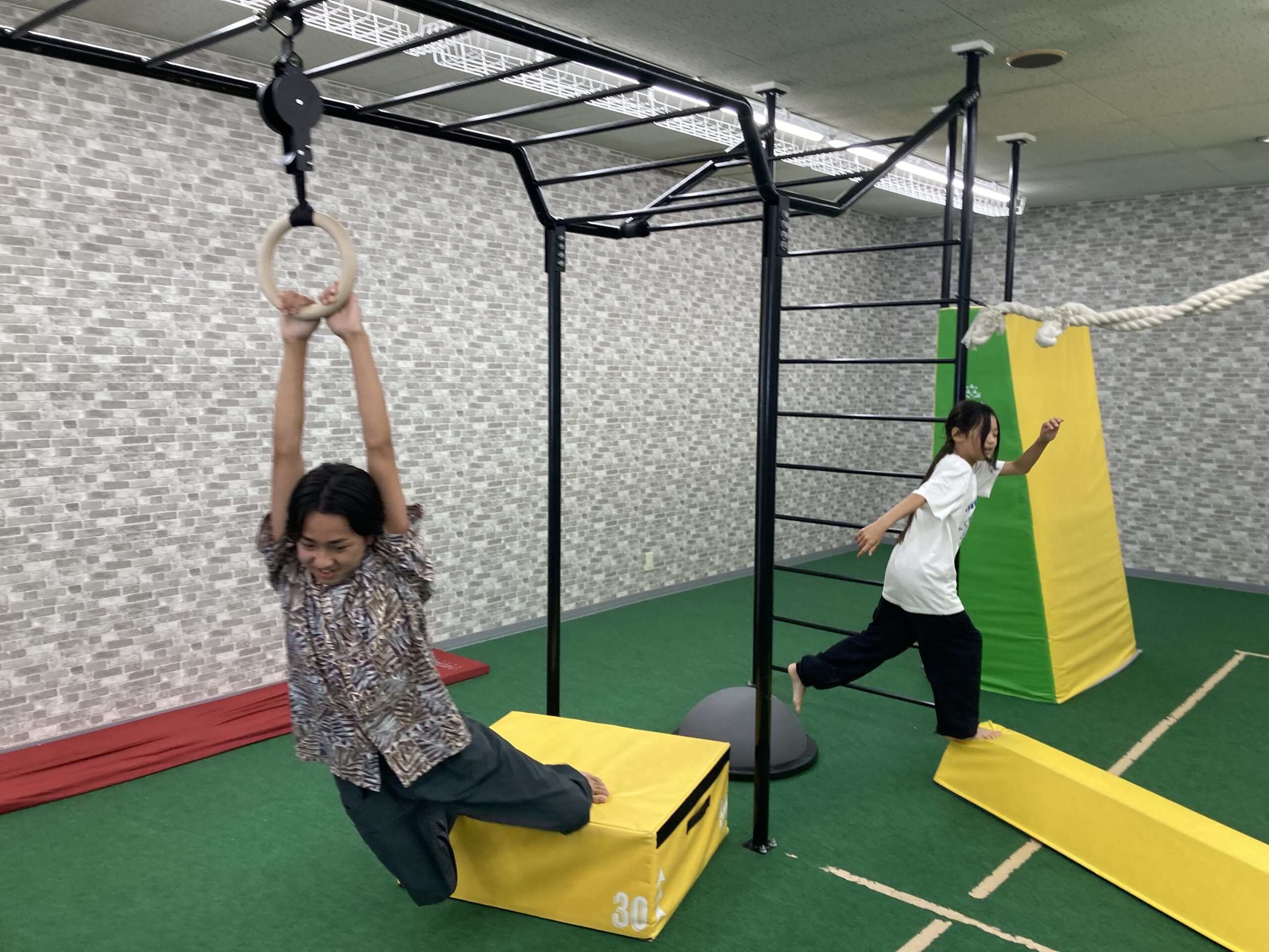 吊り輪にぶら下がる子どもと壁登りサーキットへ走る子どもの様子