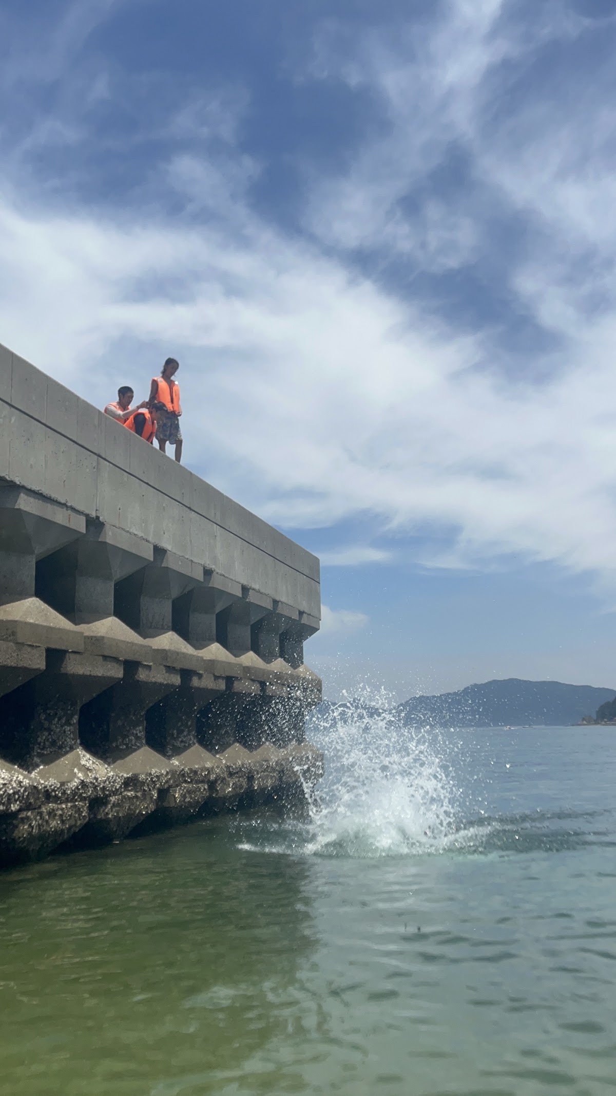 埠頭から海に飛び込んだ直後の水しぶきと見守る子どもたちの様子