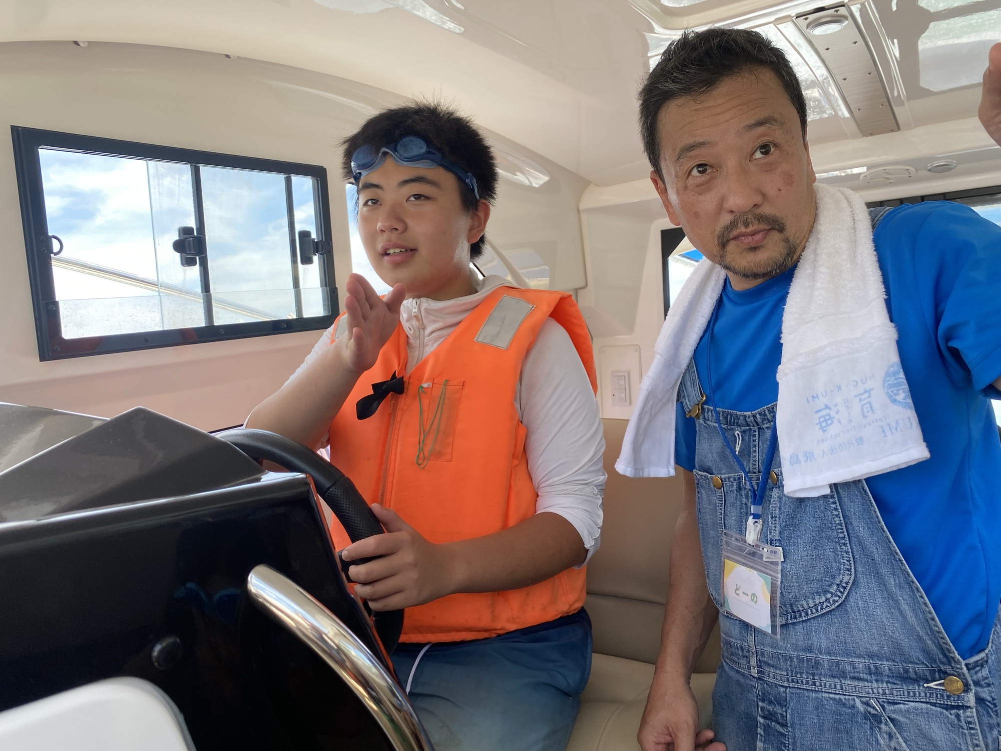 船のハンドルを握る子どもに、フリースクール育海の堂野さんが教える様子