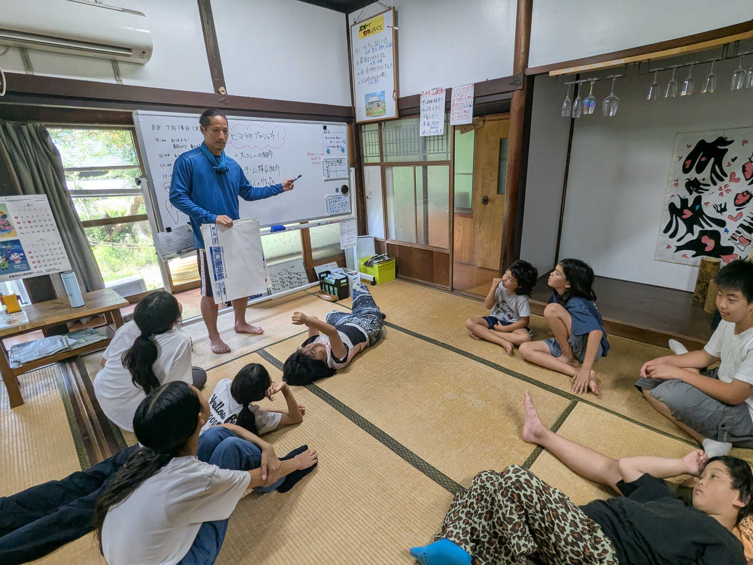 ホワイトボードの前でスタッフが説明し、子どもたちが集まって話を聞く様子