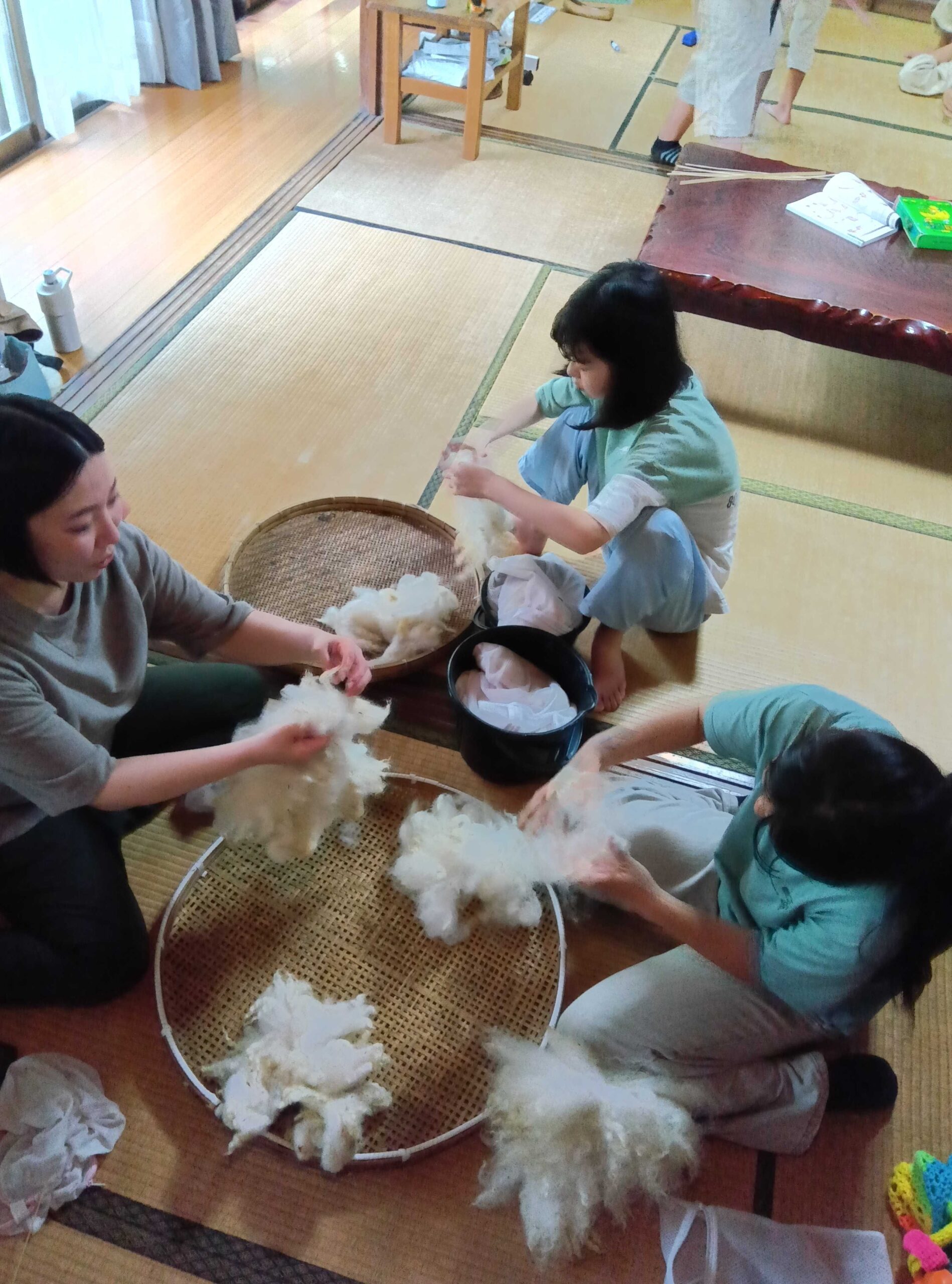 室内でスタッフと子どもたちが羊毛をほぐしながら分けている様子