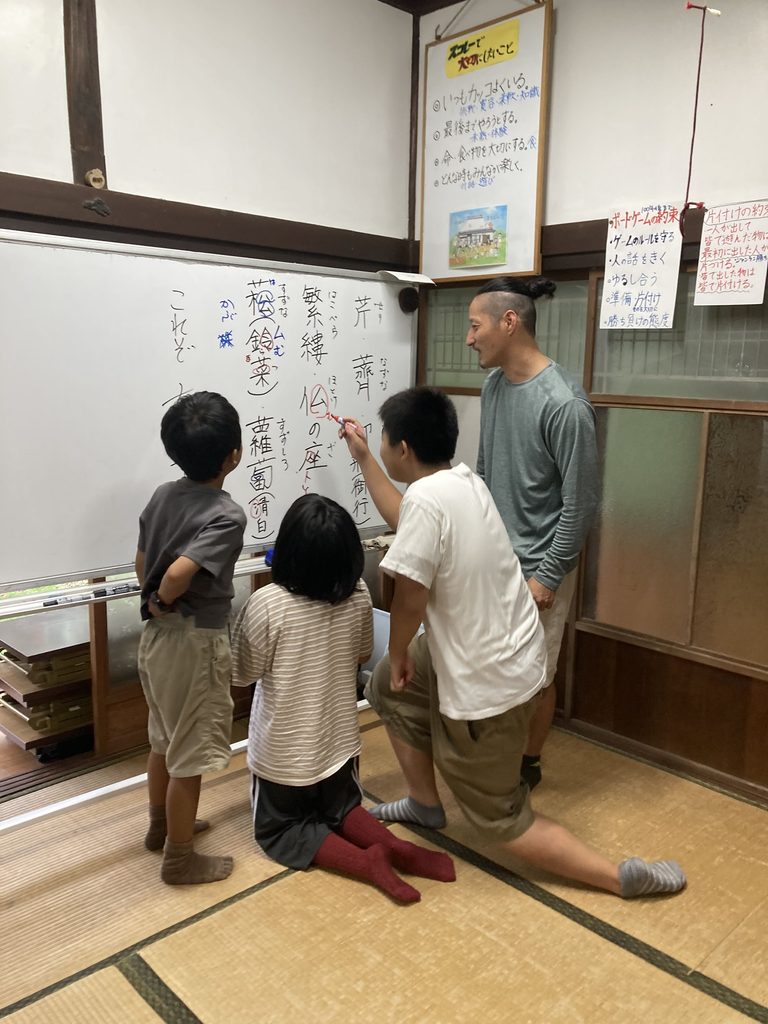 春の七草の漢字が書かれたホワイトボードを見る子どもたちとスタッフ
