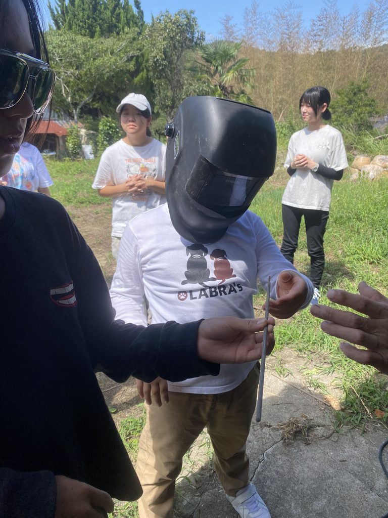 溶接マスクを試着し、道具を手渡される子ども