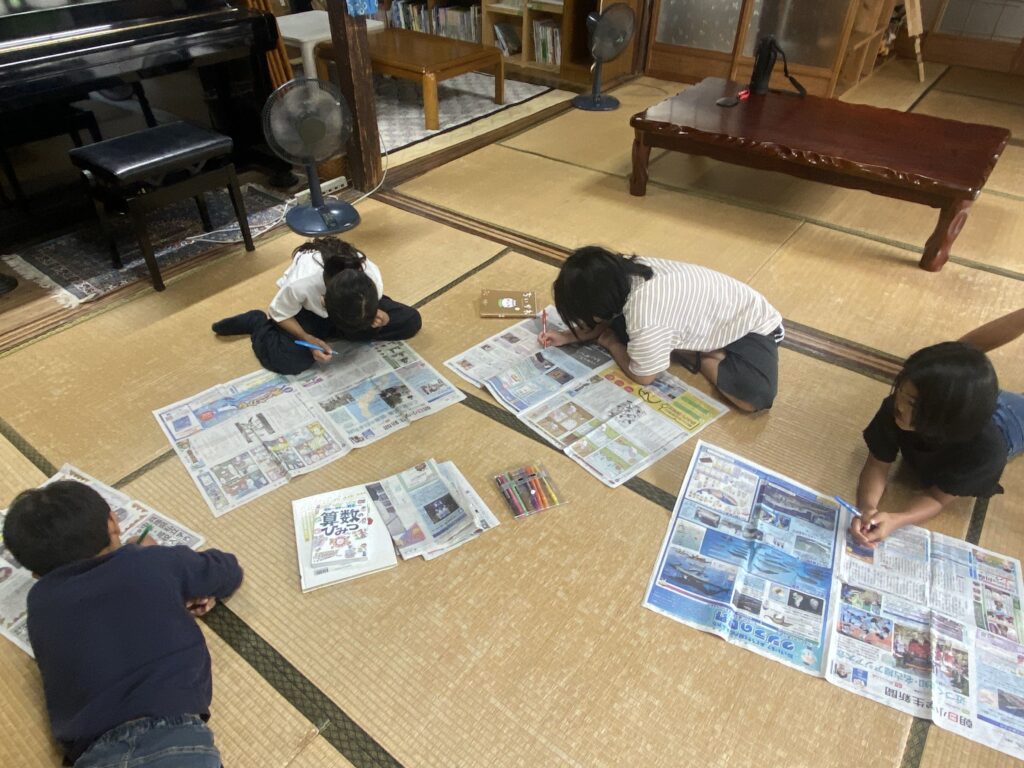 畳に新聞を広げて、漢字を探す子どもたち