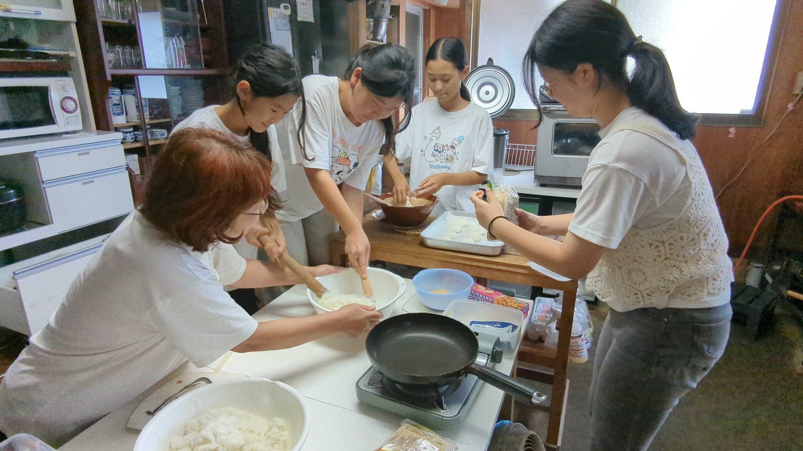 杵を使ってついたご飯をおもちに仕上げる子どもたちとスタッフの様子