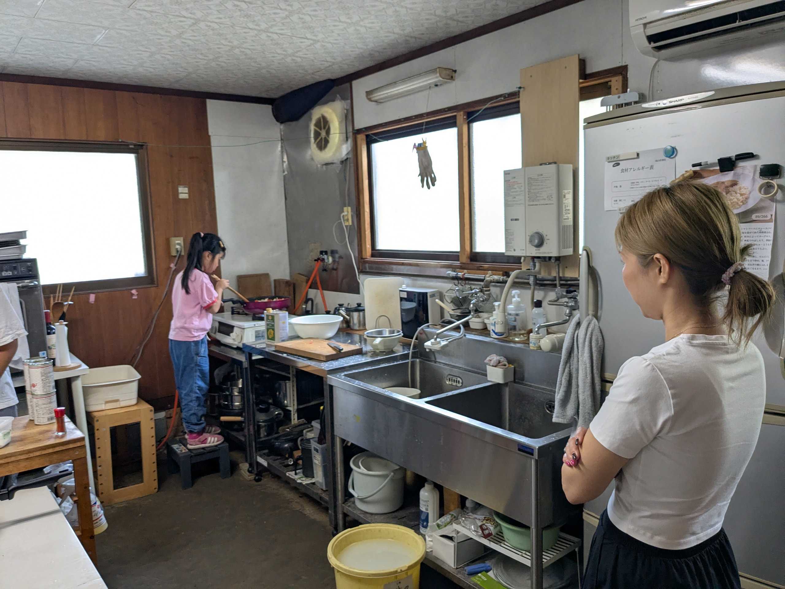 踏み台に乗って鍋の中を見ながら料理する小さい参加者とそれを見守るスタッフ