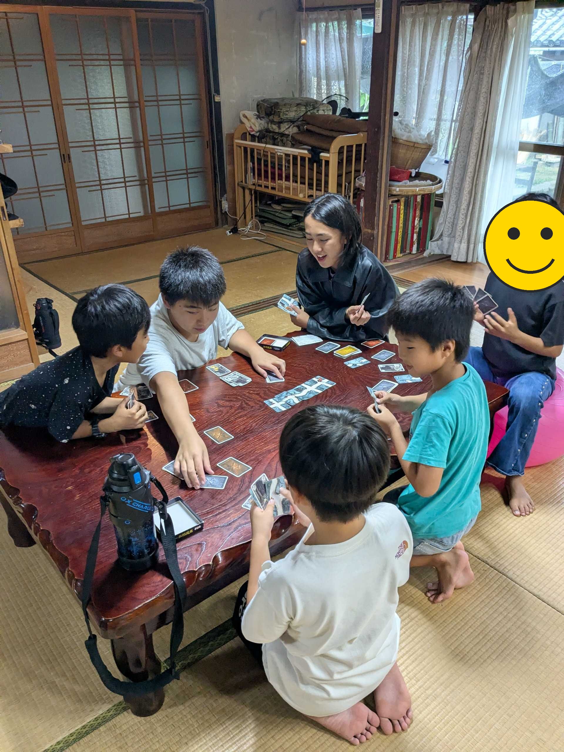 座卓を囲んでカードゲームで盛り上がる子どもたち(1人、顔にスタンプ加工)