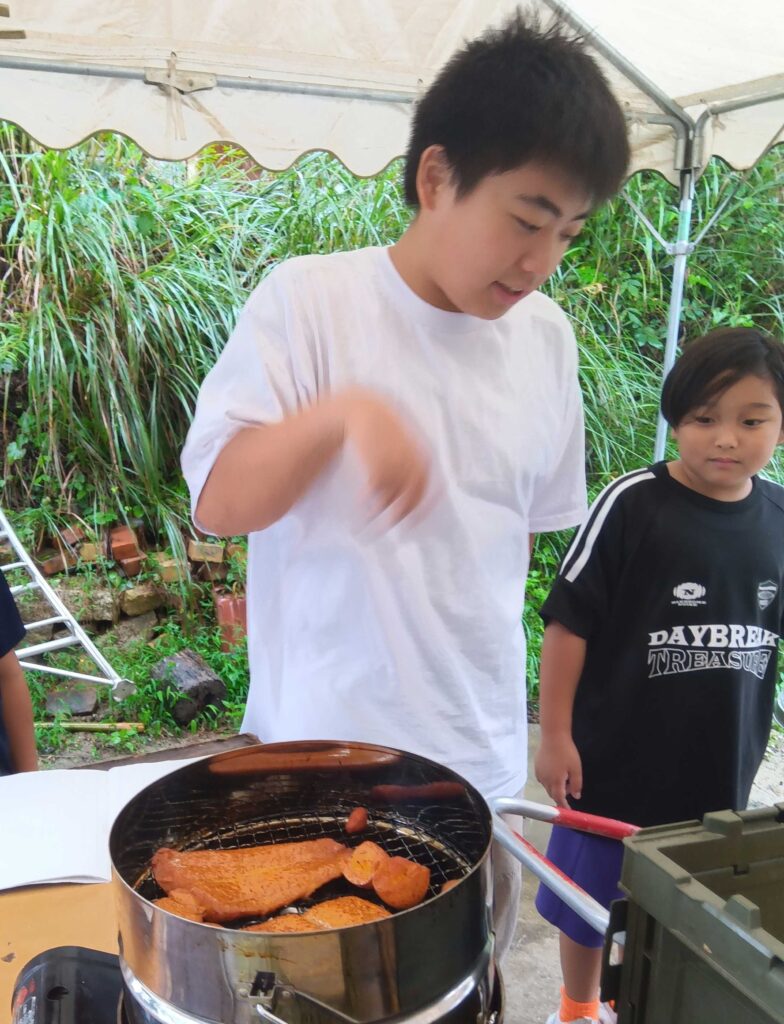 テントの下でスモーカーの中の燻製をのぞき込む子どもたち