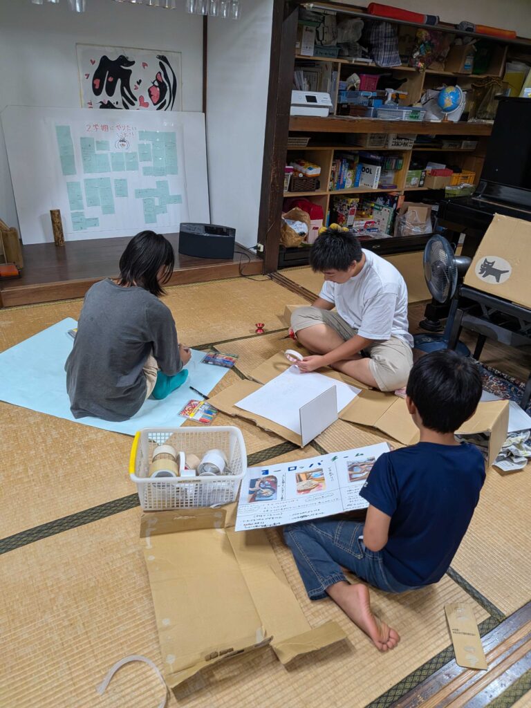 畳の上で段ボールや紙を広げて作業する子どもたち