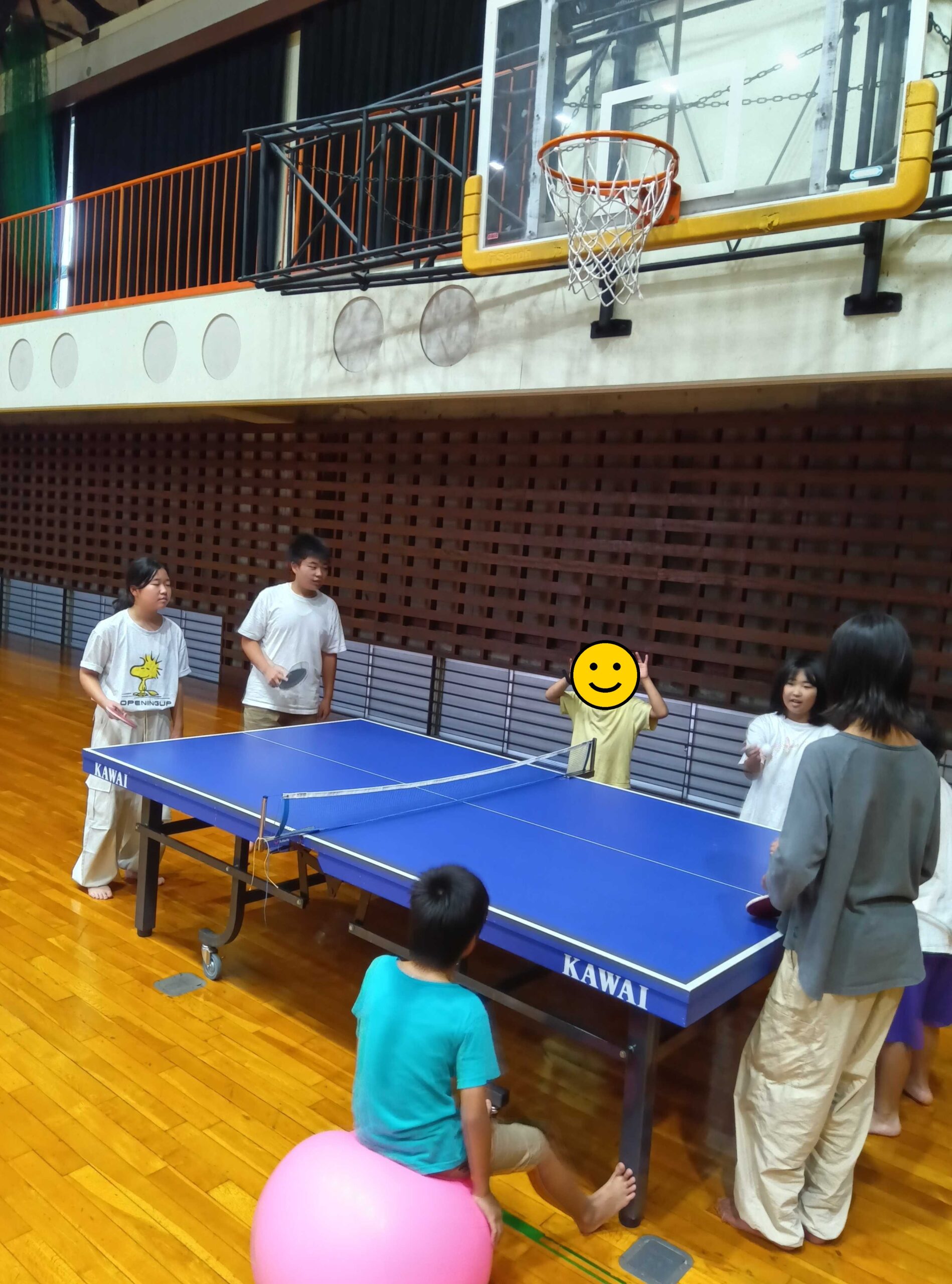 バランスボールに座る子もいる、卓球台のまわりの様子(1人、顔にスタンプ加工)