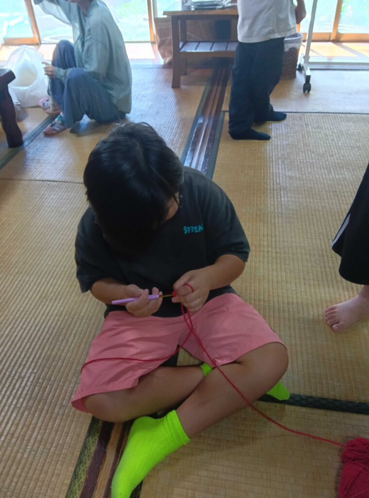 畳に座って赤い毛糸でかぎ針編みをする子