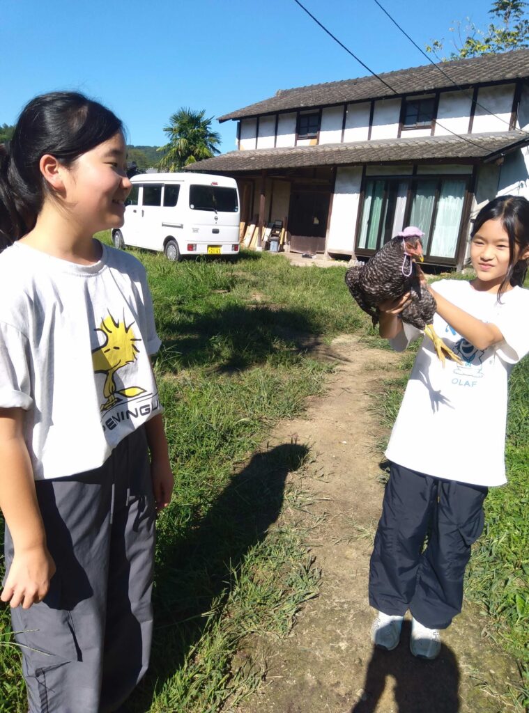 ニワトリを抱いた子と、それを見て笑う子