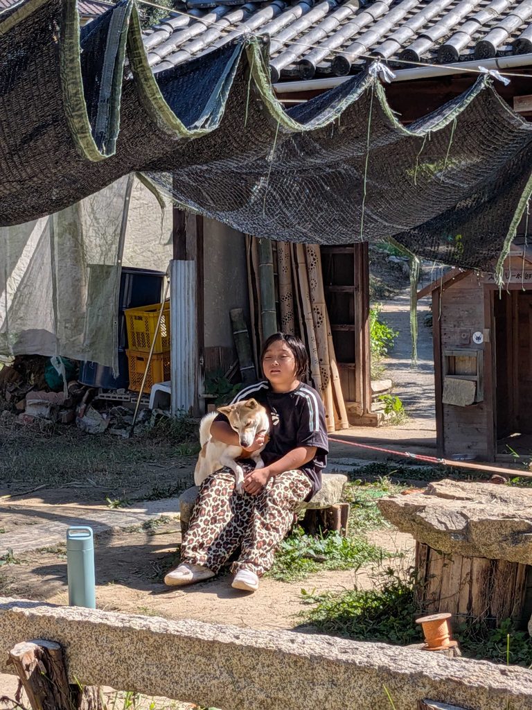 犬のサクラを抱いて、石に腰かけてくつろぐ子ども