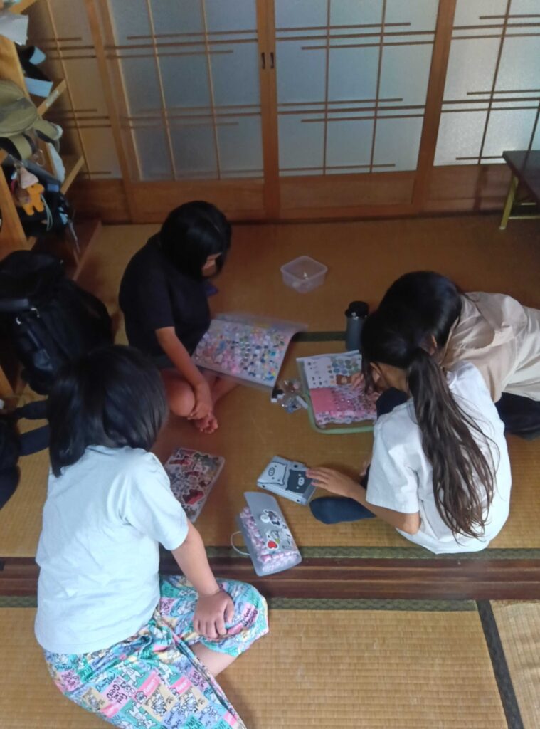 母屋の畳にシール帳を広げる子どもたち