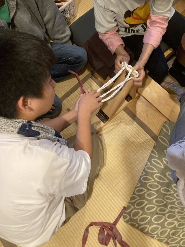 布ぞうりの編み方を、おばあちゃんの手元で教わる男の子