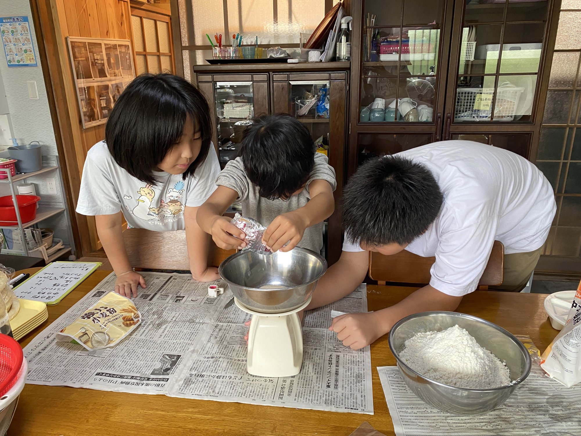 はかりで粉を量り、ピザ生地の準備をする子どもたち