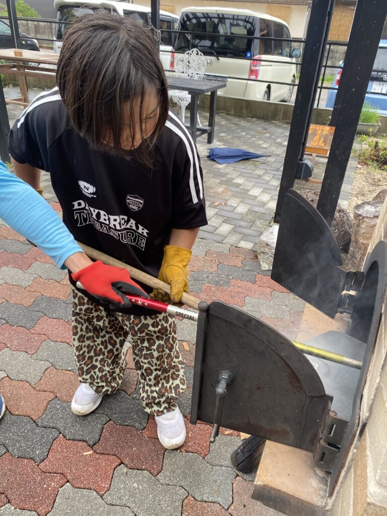 火ばさみを手に、ピザ窯の前に立つ子ども