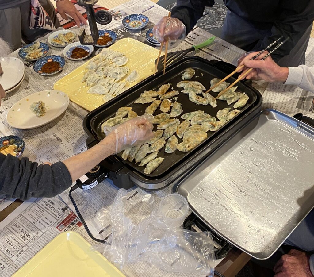 ホットプレートで焼きあがっていく餃子と、箸をのばす手