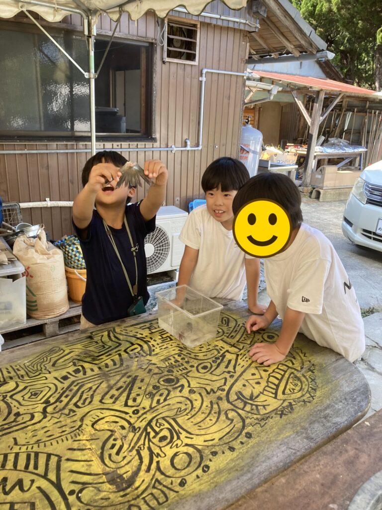 ケースの中のザリガニを手に取って見せる子どもたち（顔にスタンプ加工）