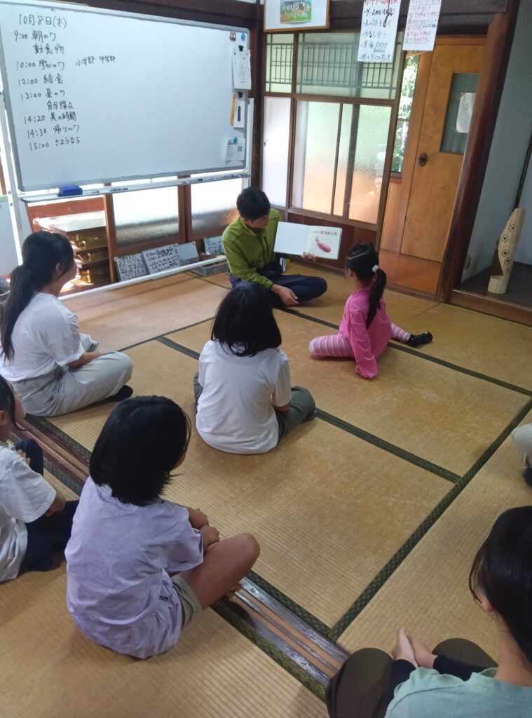 畳の部屋で、サツマイモの絵本の読み聞かせを聞く子どもたち