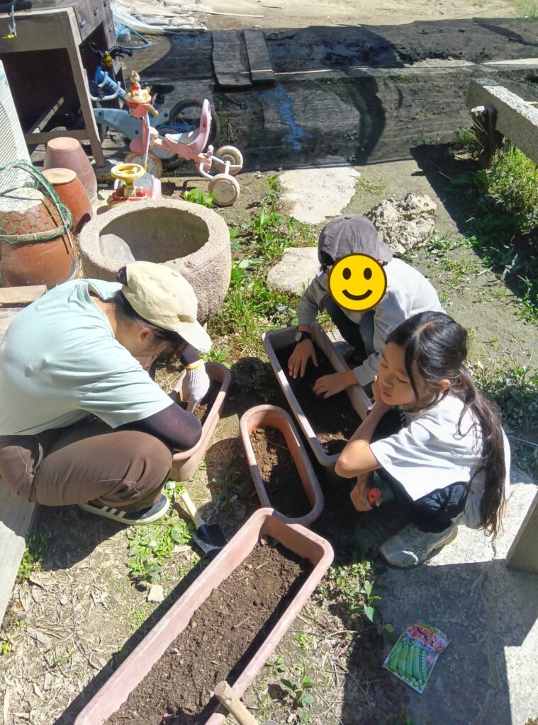 プランターの土に、エンドウの種をまく子どもたち（顔にスタンプ加工）