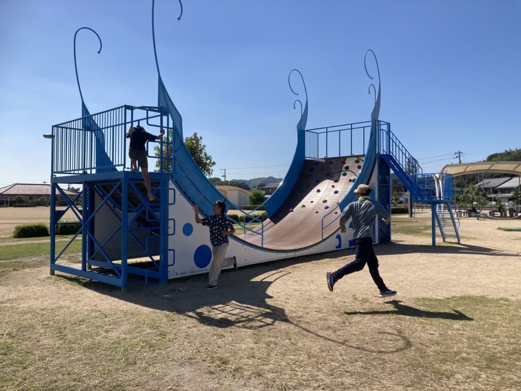 青い波の形をした大きな遊具と、そのまわりで遊ぶ子どもたち