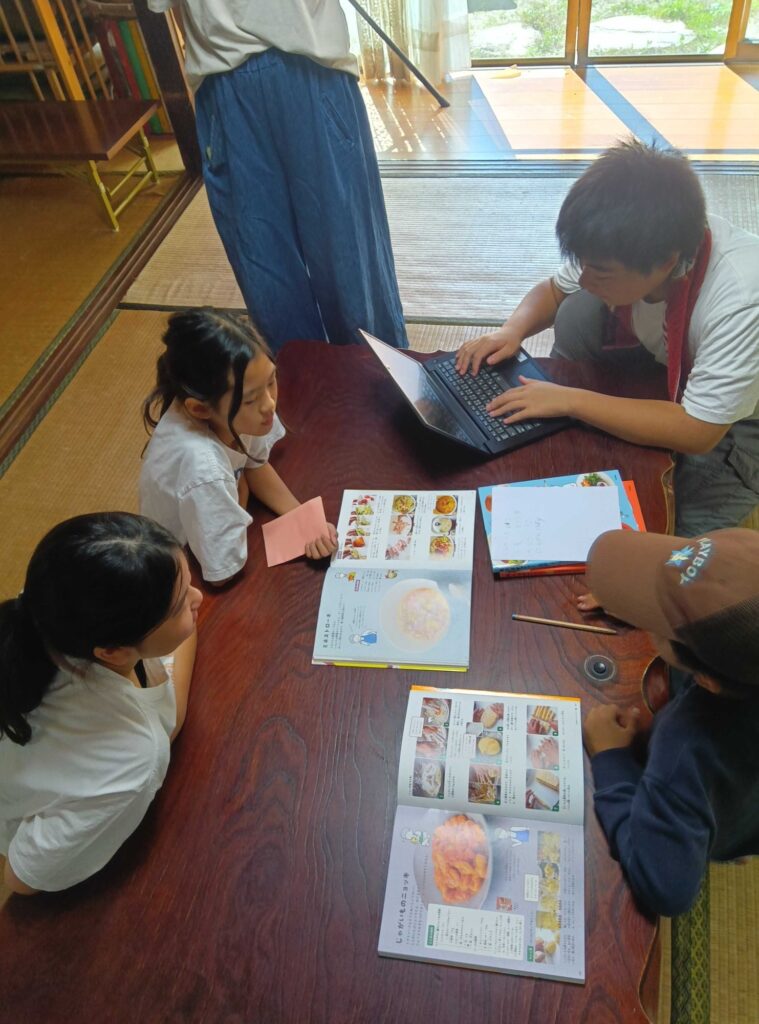 料理の本を見比べながら、パソコンに買うものを打ち込む子どもたち