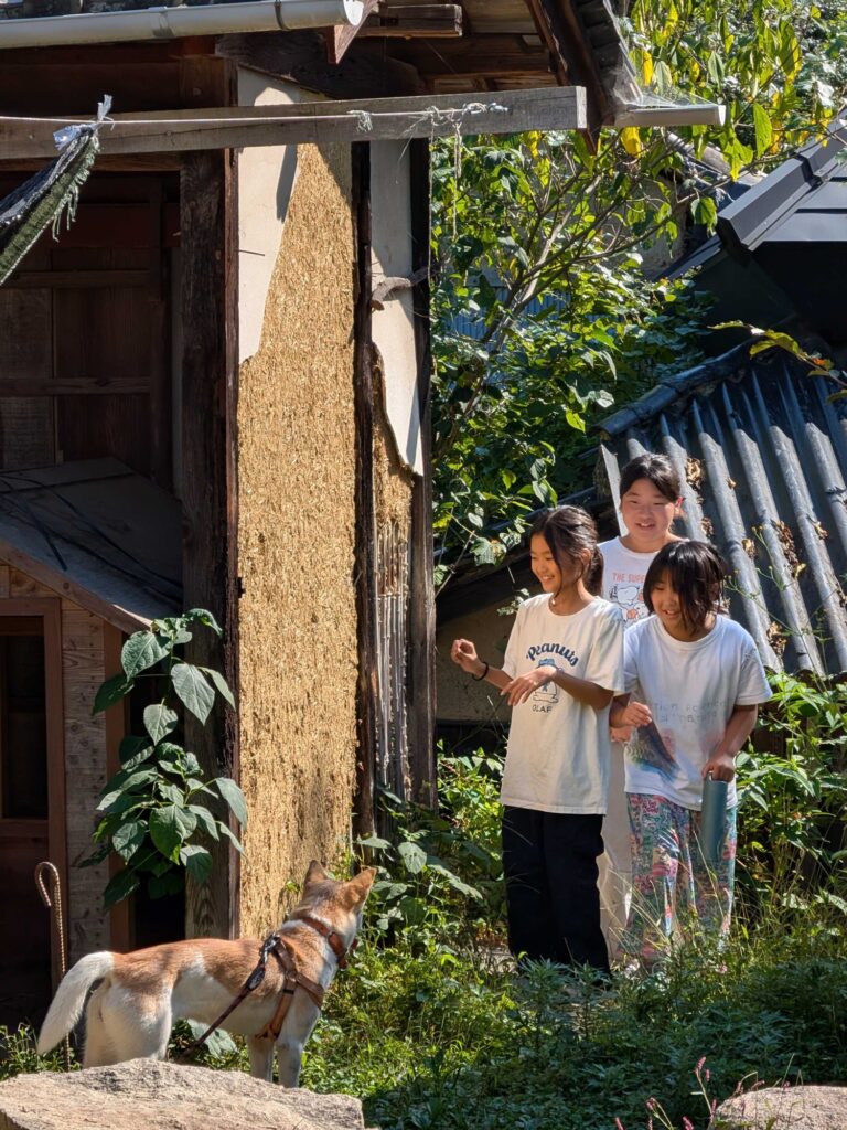小屋のそばで笑い合う子どもたちと、犬