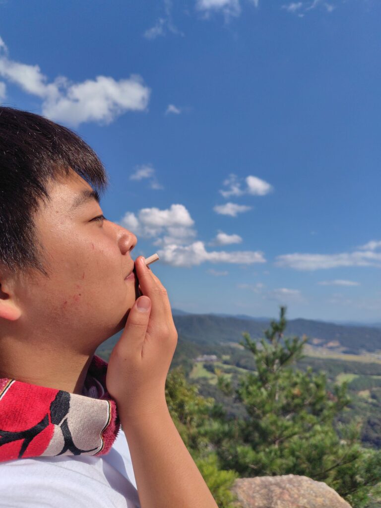 空に浮かぶ雲を、たばこの煙に見立ててポーズをとる子ども