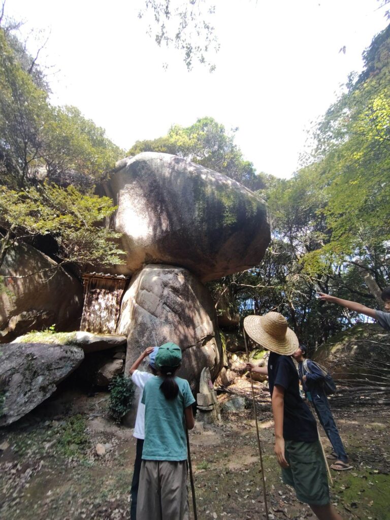 鬼の差し上げ岩を真下から見上げて、指をさす子どもたち