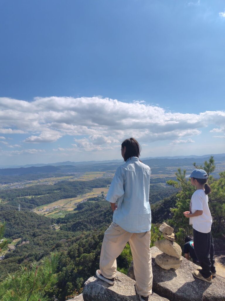岩の上に立って、眼下に広がる田んぼや町並みを眺める子どもたち