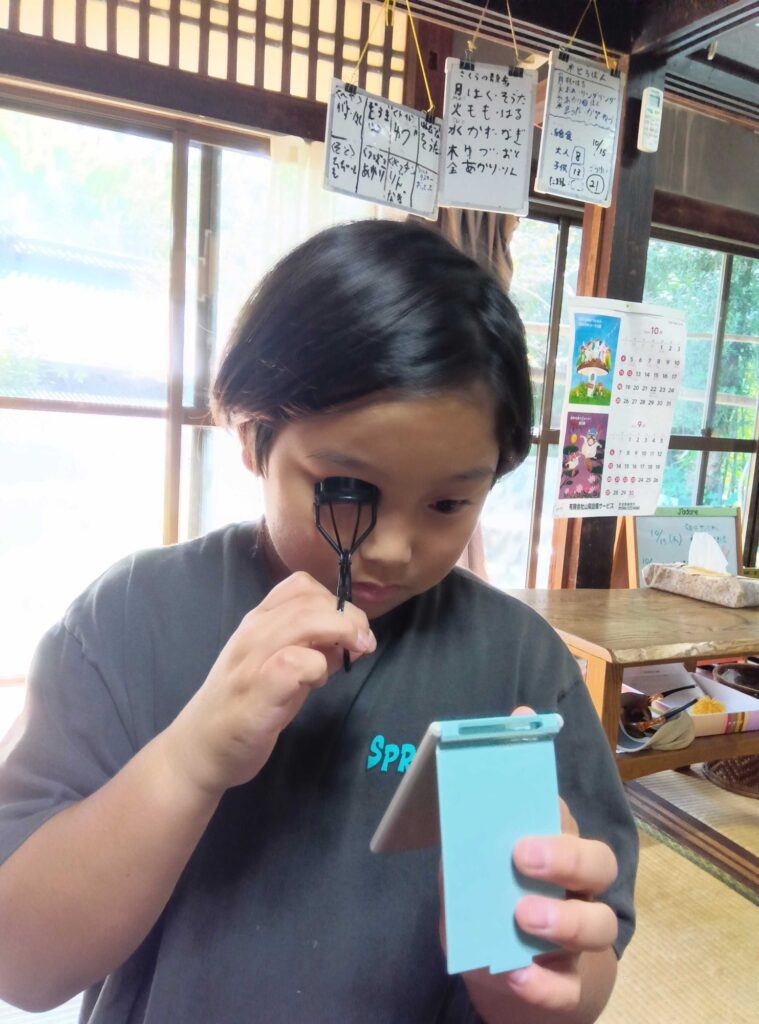 手鏡を見ながら、ビューラーでまつげを上げる子ども
