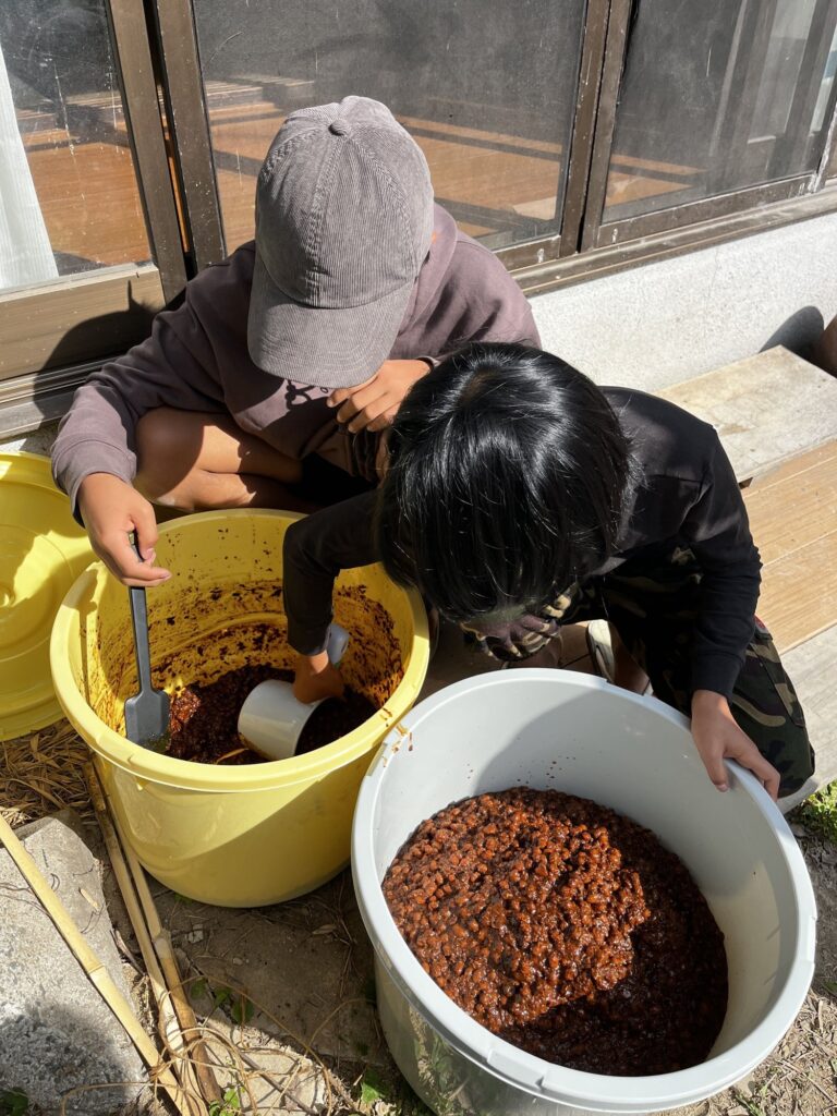 バケツに入った醤油のもろみを、かき混ぜる子どもたち