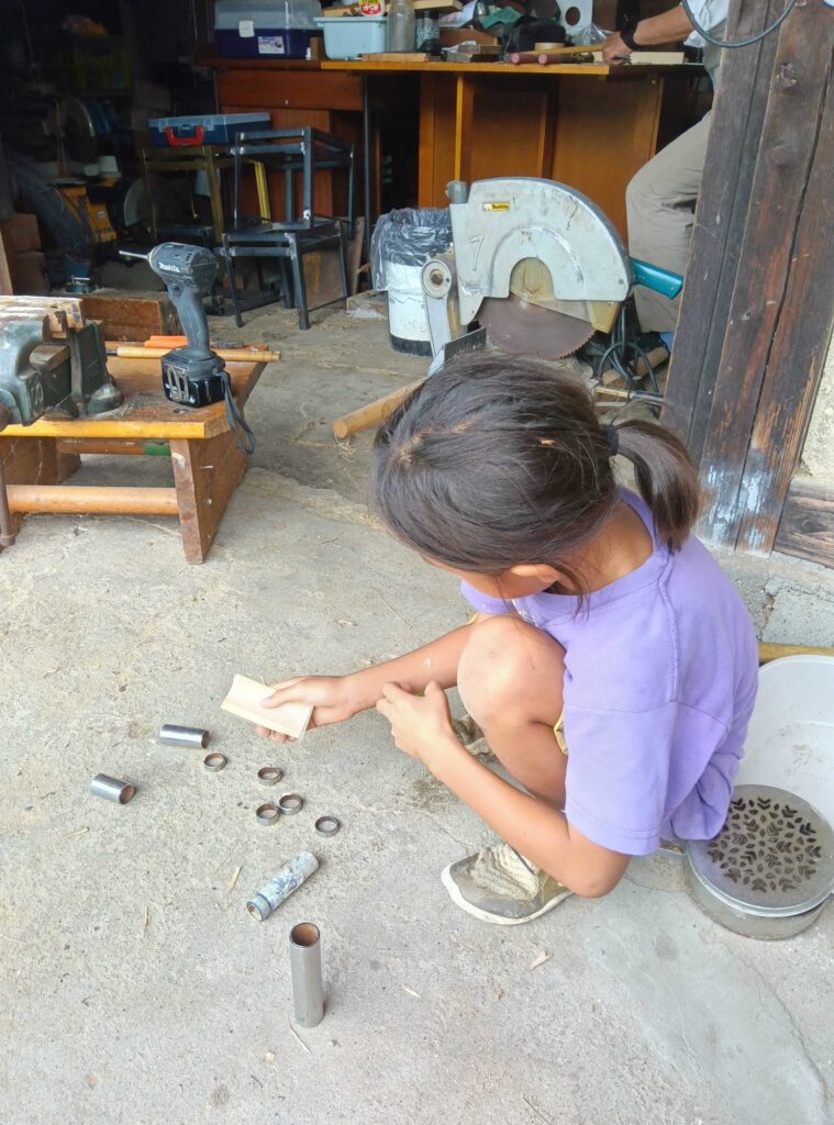 作業場の前で、銃づくりの部品を並べて作業する子ども