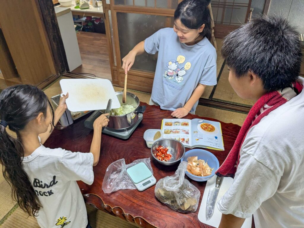 料理の本を見ながら、鍋でミネストローネを作る子どもたち