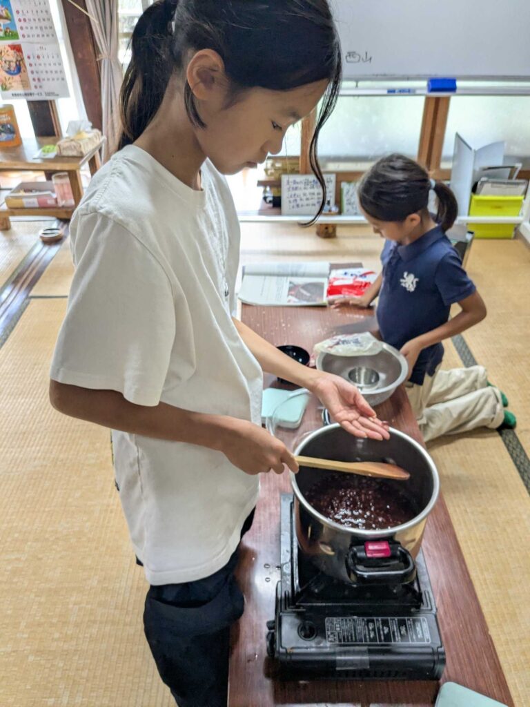 鍋の小豆を木べらで混ぜながら、つぶあんを作る子ども