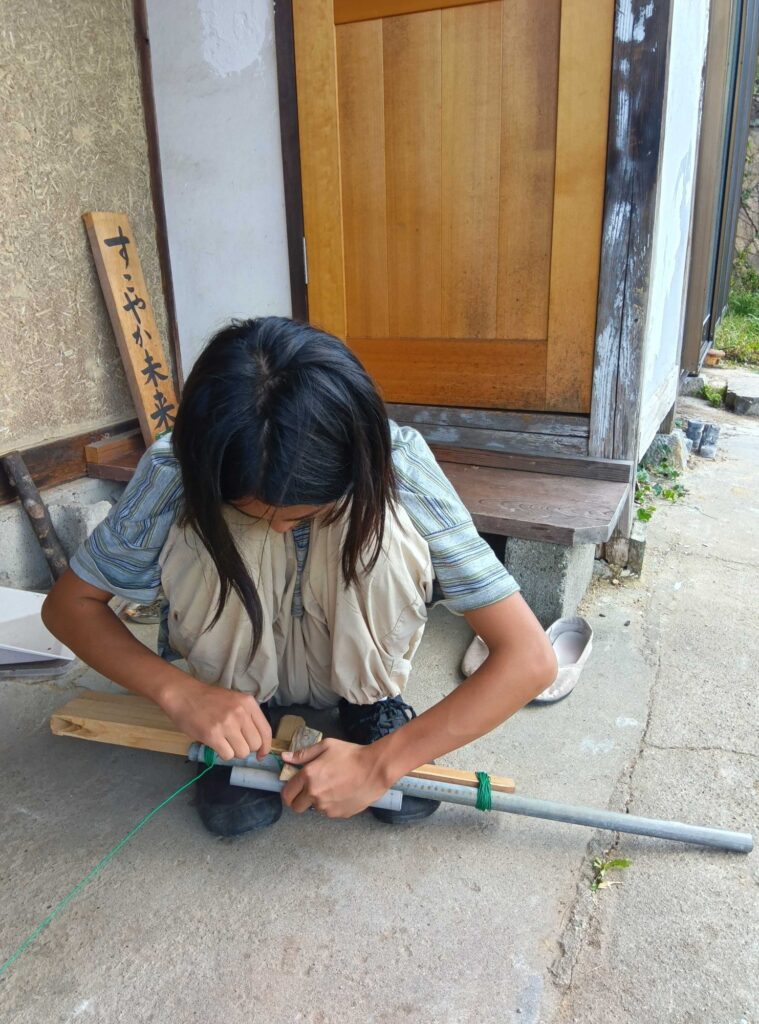 屋外でしゃがんで、パイプを使った銃を作る子ども