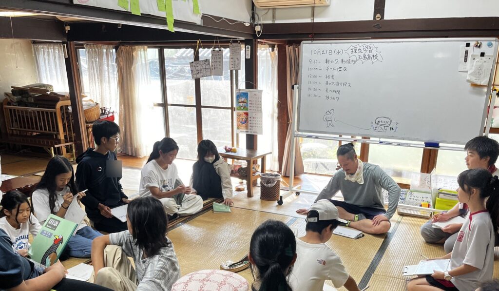 一日の予定を書いたホワイトボードの前で、輪になって座る子どもたちと高校生