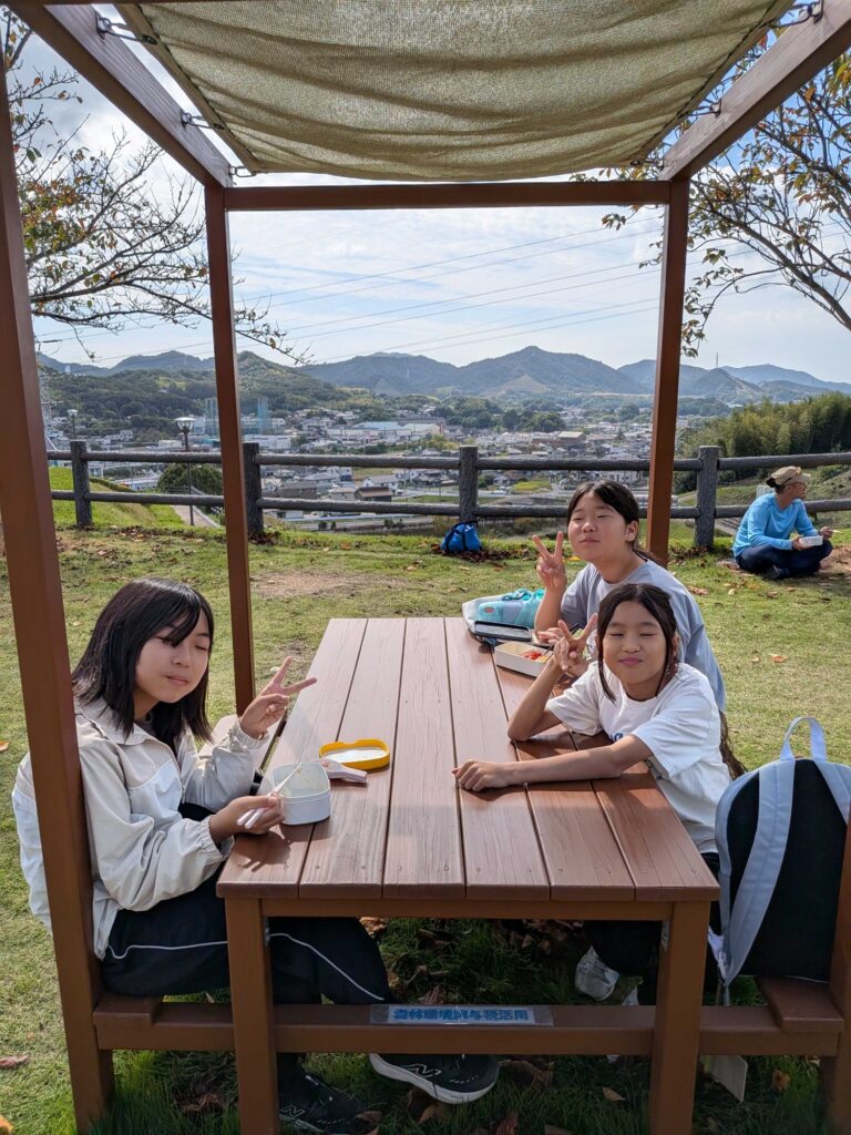 町を見下ろす屋根付きのテーブルで、お弁当を食べる子どもたち
