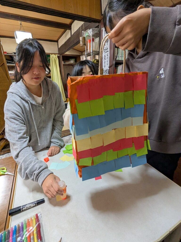 色紙を貼り重ねた紙袋のピニャータを持ち上げる子どもたち