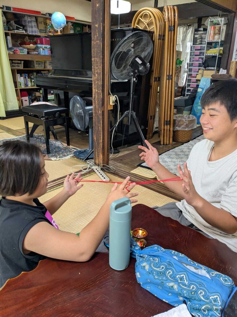 赤いひもを指にかけて、向かい合って遊ぶ子どもたち