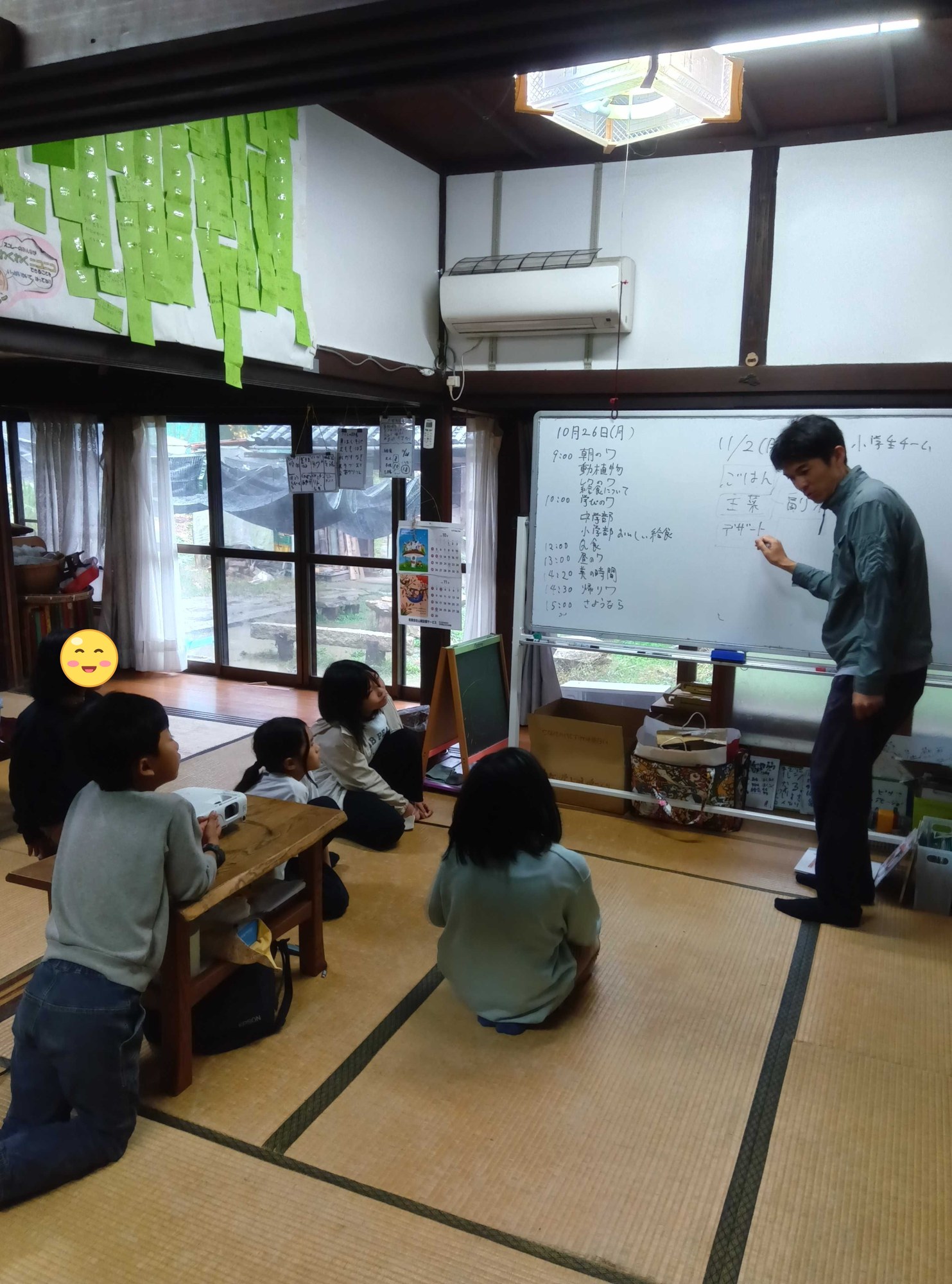 ホワイトボードに献立の枠を書くスタッフと、それを見る子どもたち