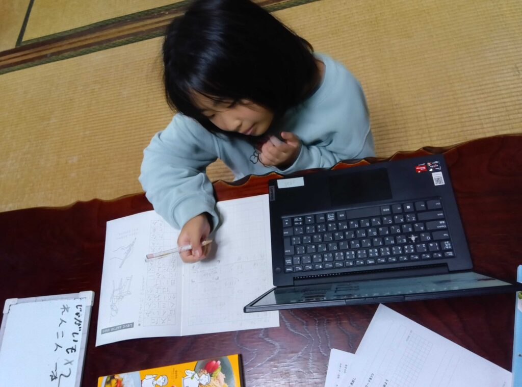 パソコンを見ながら、ノートに書き込む子ども