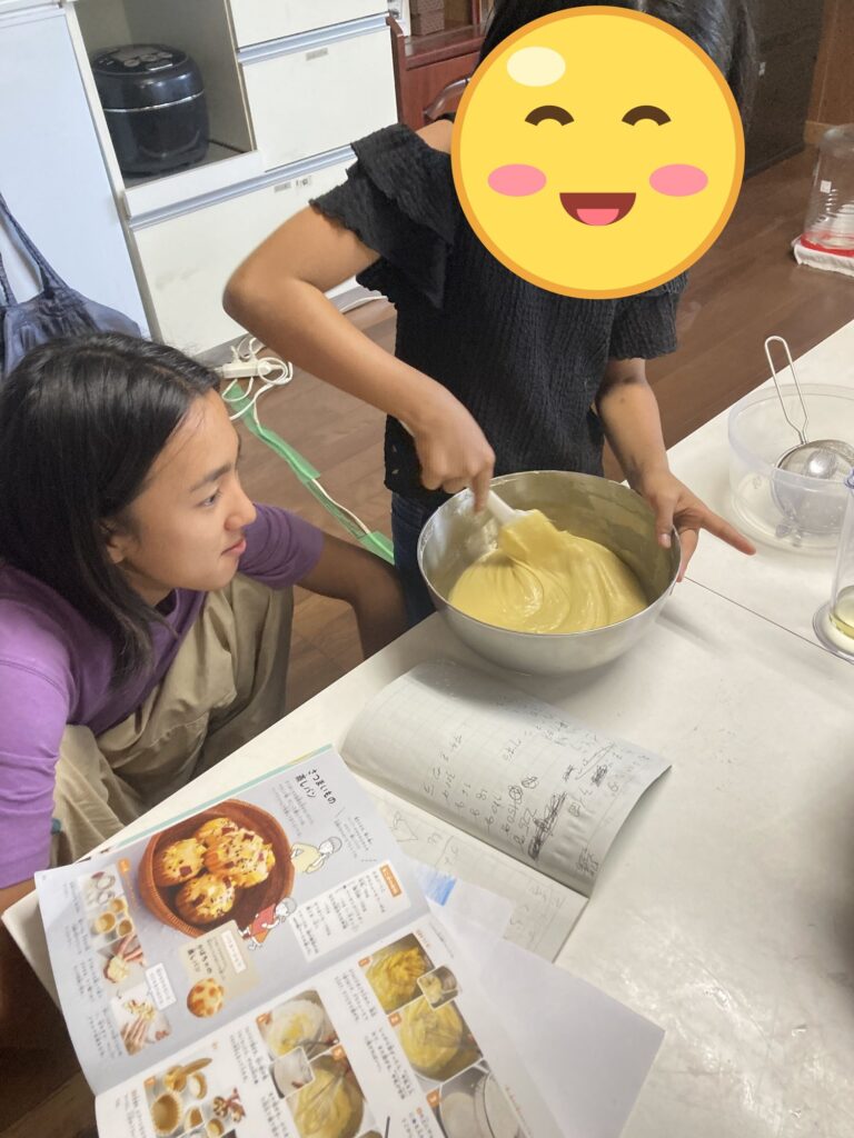 お菓子の本を見ながら、ボウルの生地を混ぜる子ども