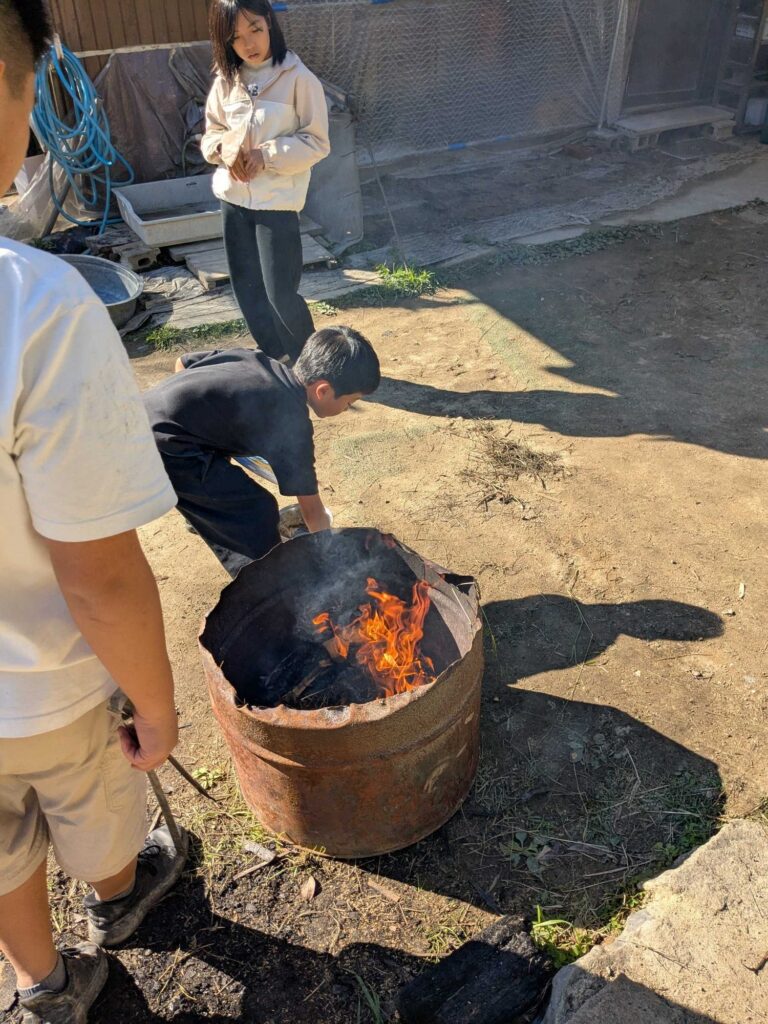 庭でドラム缶の火の様子を見る子どもたち